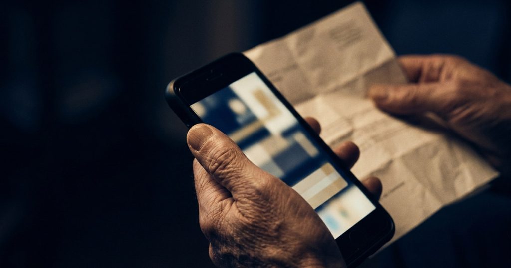 Mãos segurando o celular com um aviso na tela e uma carta em papel