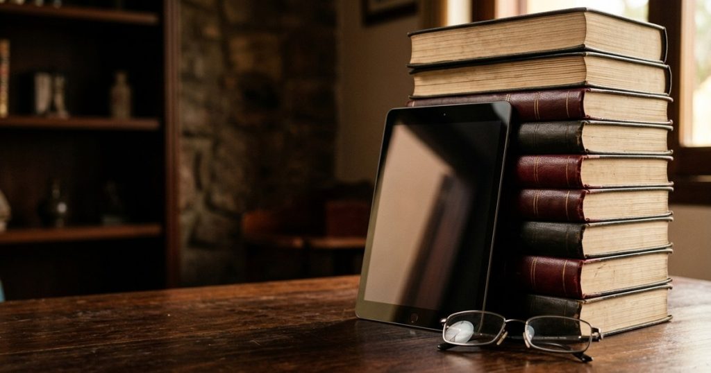 Pilha de códigos legais e tablet sobre mesa de madeira, representando as leis da reforma tributária